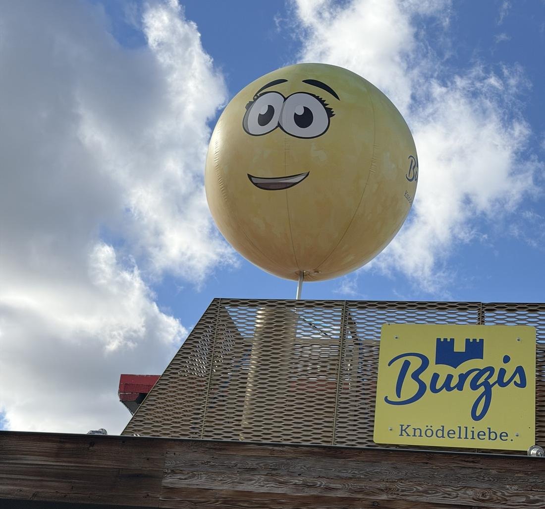 Großer Knödel-Ballon mit Gesicht über dem Burgis-Schild