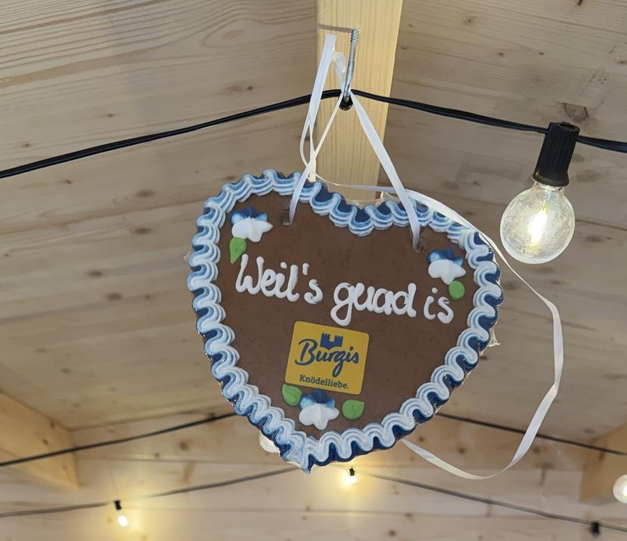 Lebkuchenherz „Weil’s guad is“ mit Burgis-Logo in der Holzhütte